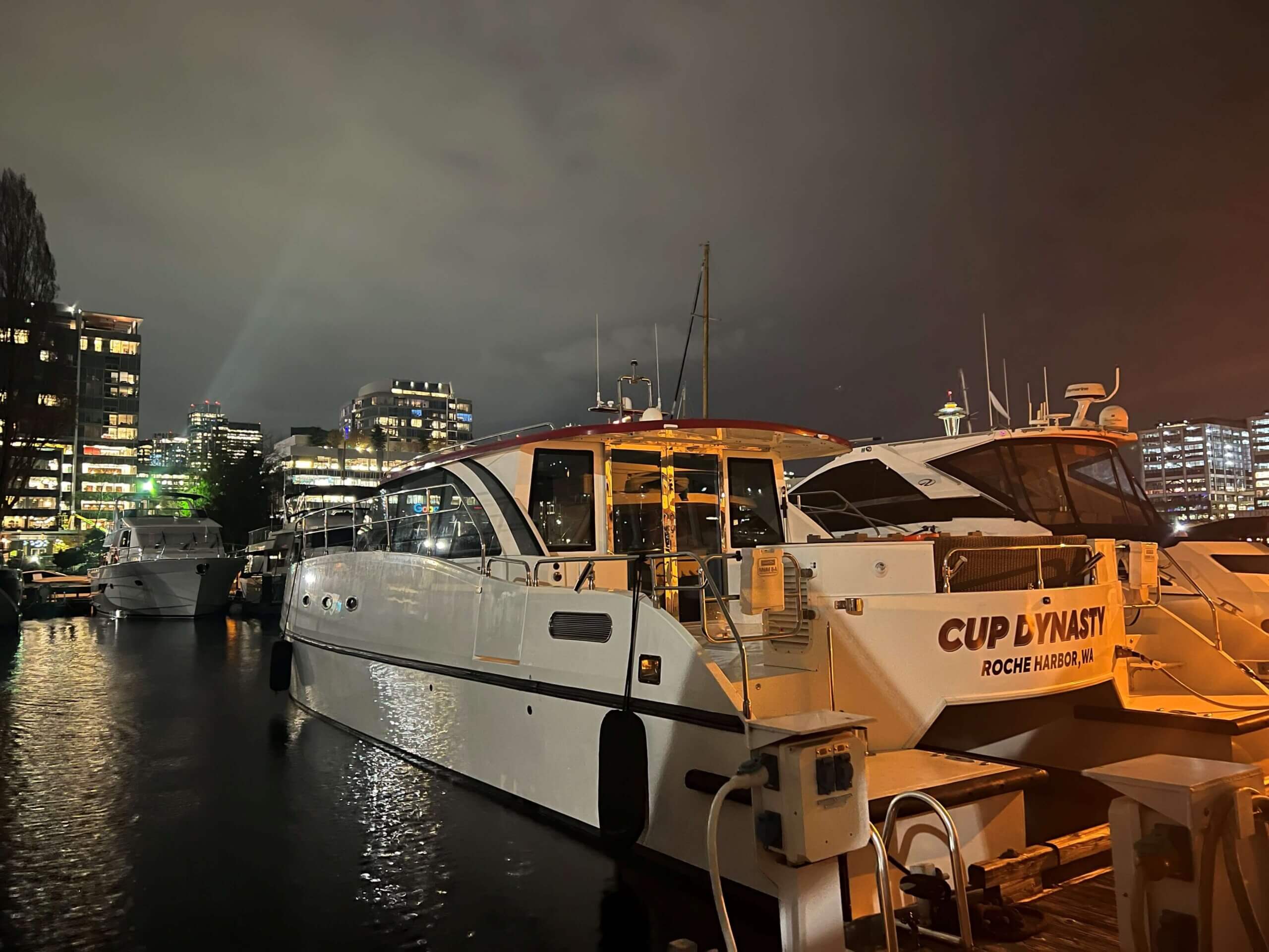 CDLLC - Cup Dynasty Catamaran at night docked in a city port with buildings on the horizon